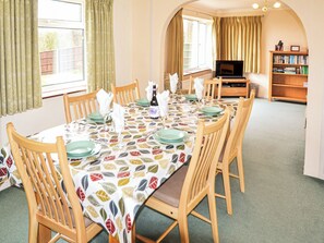 A dining area with a table set for six, wooden chairs, a television in the background, and a bookshelf. - 4 bedroom accommodation in St Lawrence (St Lawrence)