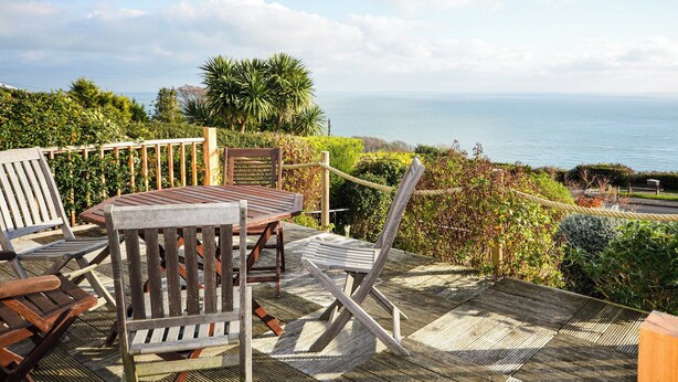 A wooden deck with a table and chairs overlooking a coastal view. - Bonito is situated in Ventnor with panoramic sea views. (Ventnor)