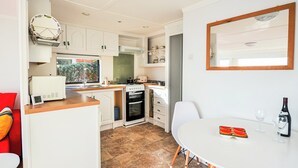 A compact kitchen with white cabinets, a stove, and a sink. There is a dining table with a chair and a bottle of wine. - Bonito is situated in Ventnor with panoramic sea views. (Ventnor)
