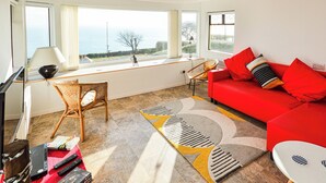 A modern living room with a red sofa, a wicker chair, and a view of the sea through large windows. - Bonito is situated in Ventnor with panoramic sea views. (Ventnor)