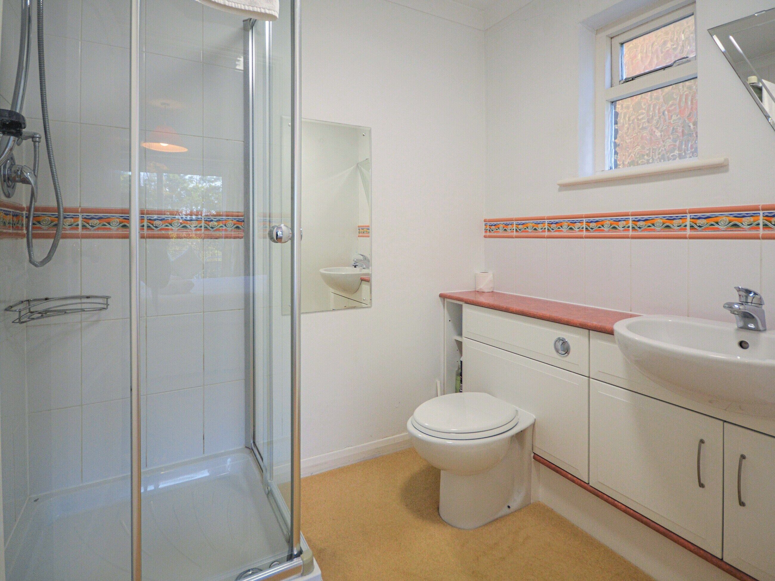 A bathroom with a glass shower enclosure, a toilet, a sink, and a mirror.