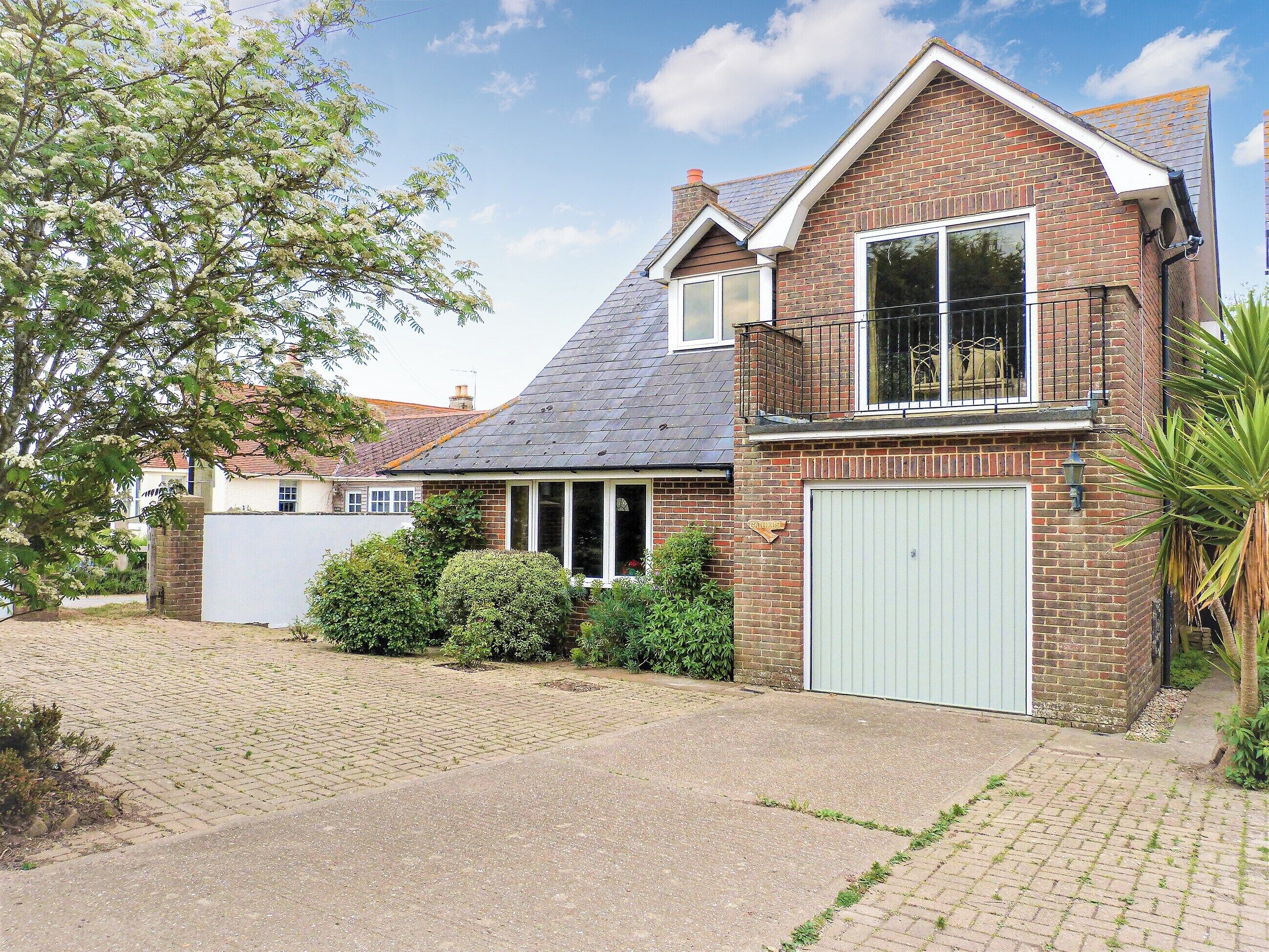 A two-story house with a brick facade, a garage, and a small garden area with a tree and shrubs.