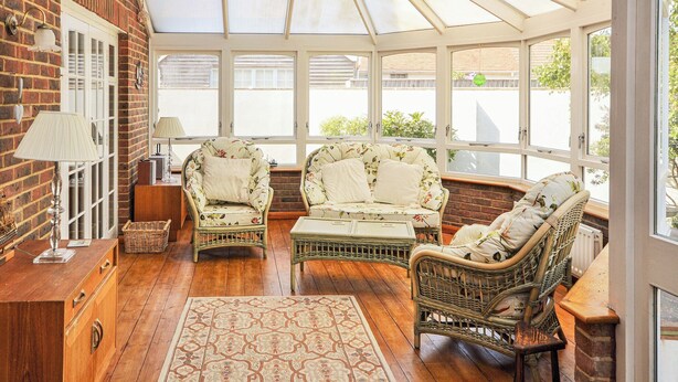 Un solárium con muebles de mimbre, un armario de madera y una alfombra estampada.