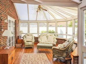 A sunroom with wicker furniture, a wooden cabinet, and a patterned rug. - 3 bedroom accommodation in Bembridge (Bembridge)