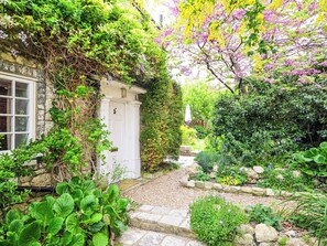 Un chemin de pierres menant à une porte blanche, entourée d’une végétation luxuriante et de plantes en fleurs.