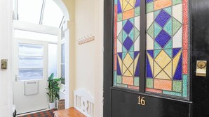 Un pasillo con piso de cuadros, un banco, una puerta con un vitral colorido y una vista a través de la puerta.
