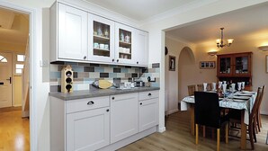 A modern kitchen with white cabinets, a tiled backsplash, and a dining area with a table set for four. - 4 bedroom accommodation in Ryde (Ryde)