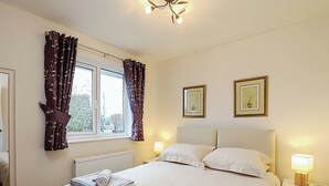 A neatly made bed with two pillows, a bedside table with a lamp, and a window with curtains. - 4 bedroom accommodation in Ryde (Ryde)