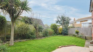 A well-maintained backyard with a grassy lawn, a palm tree, and a stone pathway leading to a house. - 4 bedroom accommodation in Ryde (Ryde)