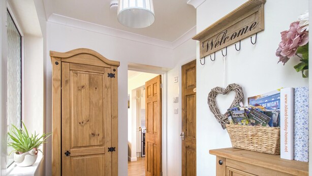 Corredor com portas de madeira, um cesto de vime com revistas e uma placa de 'Welcome'.