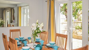 Un coin repas avec une table en bois dressée pour six personnes, de la vaisselle bleue et un vase contenant des fleurs blanches.
