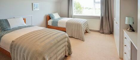 Un dormitorio con dos camas, una ventana con cortinas, un radiador y un aparador con cajones.