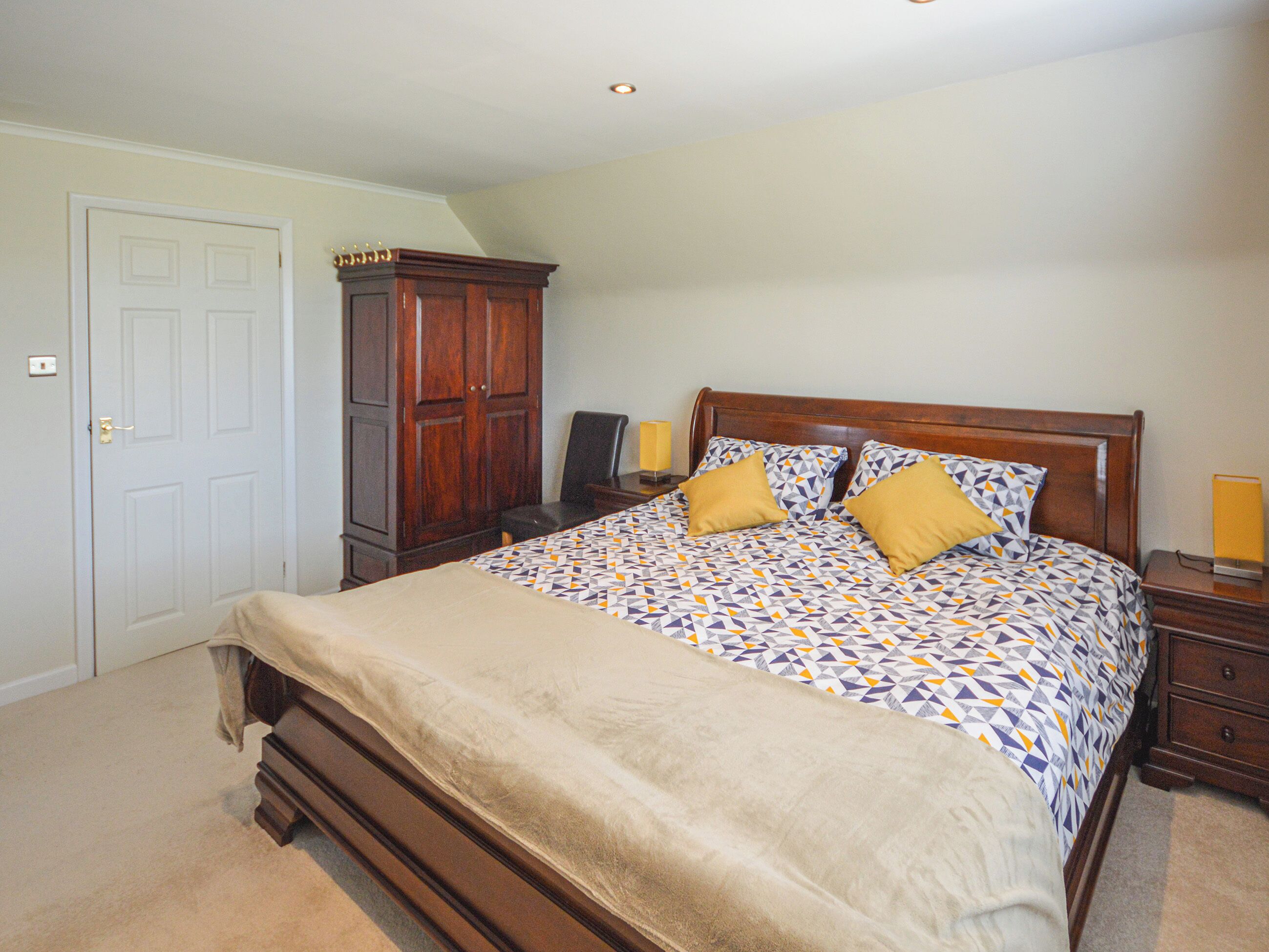 A bedroom with a bed, wooden wardrobe, and bedside tables.