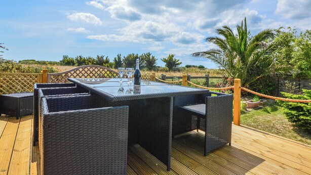 Une terrasse extérieure avec une table à plateau de verre, des chaises en osier et une bouteille de champagne.