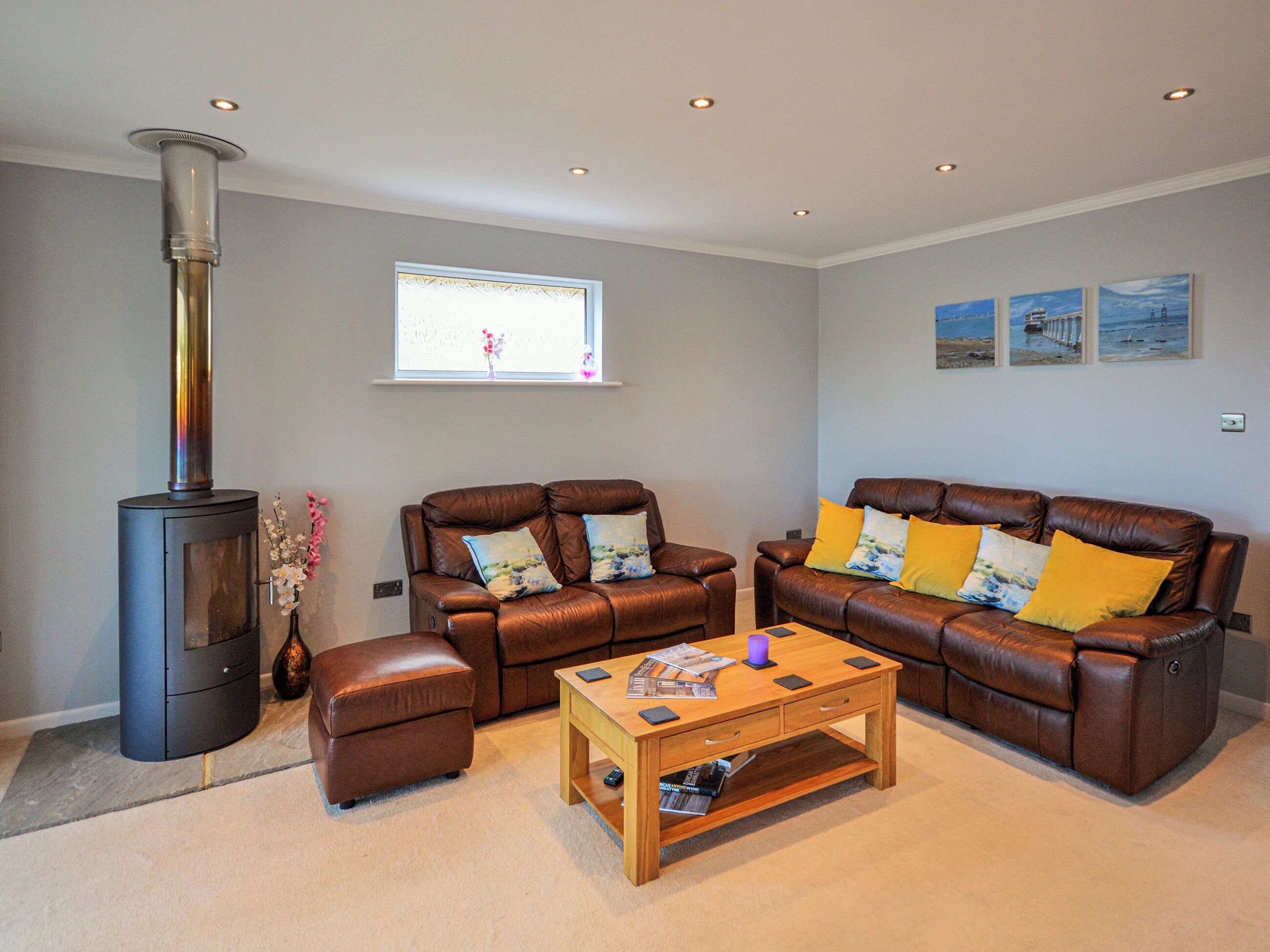 A living room with a wood-burning stove, two leather sofas with cushions, a wooden coffee table, and a window with a view of the outdoors.