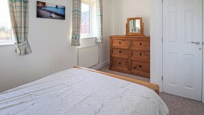 Quarto com cama, penteadeira, espelho e janela com cortinas.