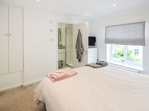 Ein Schlafzimmer mit einem Bett, einem Fernseher, einem Fenster mit Blick, einem Kleiderschrank und einem durchgehenden Türspalt sichtbaren Badezimmer.