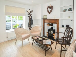 Ein gemütliches Wohnzimmer mit Korbstühlen, einem Couchtisch mit Zeitschriften, einem Kamin mit Holzscheiten und einer herzförmigen Dekoration an der Wand.