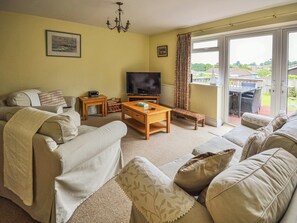 A living room with a sofa set, a television, a wooden coffee table, and a view of the outdoors through a sliding glass door. - 3 bedroom accommodation in Seaview (Seaview)