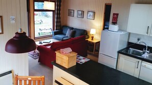 Ein kompakter Wohnbereich mit Küchenzeile, einer Couch, einem Esstisch und einem Fenster mit Blick auf einen Garten.