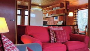 Un interior de cabaña acogedor con un sofá rojo, un sillón azul y techo de madera.
