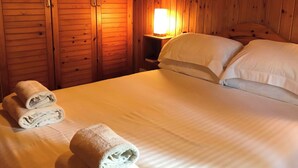 Una habitación con paneles de madera, una cama, almohadas y una mesita de noche con una lámpara.