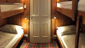 Una habitación con cuatro literas, piso a cuadros y una puerta con interruptor de luz.