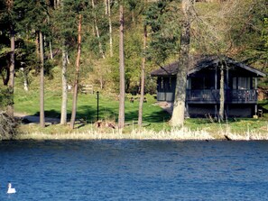 A lakeside cabin with a dock, surrounded by tall trees and a grassy area. - Cedar Chalet 19 - UKC5237 (Crieff)