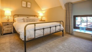 Een slaapkamer met een bed, twee nachtkastjes, lampen, een raam met gordijnen en een schuine kap.