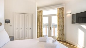 A hotel room with a bed, a TV, a wardrobe, and a view of a body of water through the curtains.