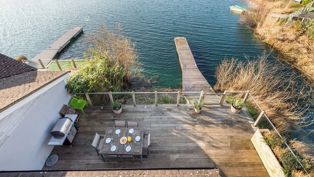 A wooden deck with a table set for dining, overlooking a calm river.