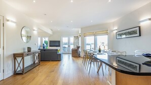 A spacious kitchen with wooden flooring, a dining area with chairs, a large mirror, and a television.