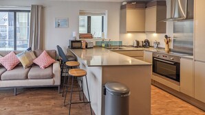 Una cocina moderna con una isla central, electrodomésticos integrados y un comedor con sofá y taburetes de bar.