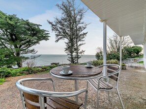 A patio with a table and chairs overlooking a body of water, surrounded by trees and greenery. - 7 Mount Brioni - UKC5342 (Torpoint)