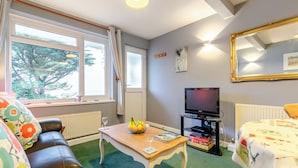 Ett vardagsrum med en soffa, ett soffbord, en tv och ett fönster med gardiner.