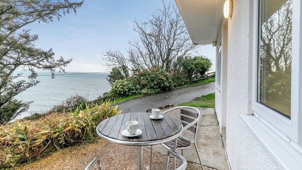 A patio with a table and chairs overlooking a body of water, with a pathway leading to a house. - 8 Mount Brioni - UKC5343 (Torpoint)