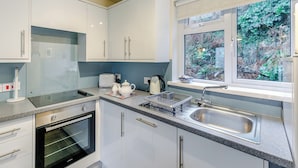 Een moderne keuken met witte kasten, een inbouwoven, een gootsteen en een raam met uitzicht op groen.