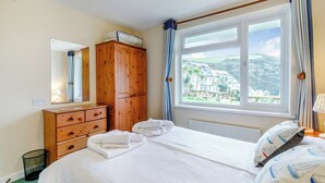 Een slaapkamer met een groot bed, een houten garderobe, een spiegel en een raam met uitzicht op huizen en begroeiing.