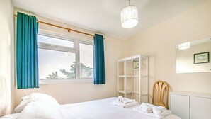 Un lit bien fait, avec du linge de lit blanc, une fenêtre ornée de rideaux bleus, une armoire blanche et un miroir accroché au mur.