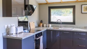 A modern kitchen with dark cabinets, a built-in oven, a sink, and a window with blinds. - 2 bedroom accommodation in Stanton-On-The-Wolds (Stanton-On-The-Wolds)