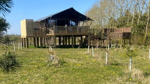 A wooden cabin with a deck, surrounded by a fenced area and trees. - 2 bedroom accommodation in Stanton-On-The-Wolds (Stanton-On-The-Wolds)
