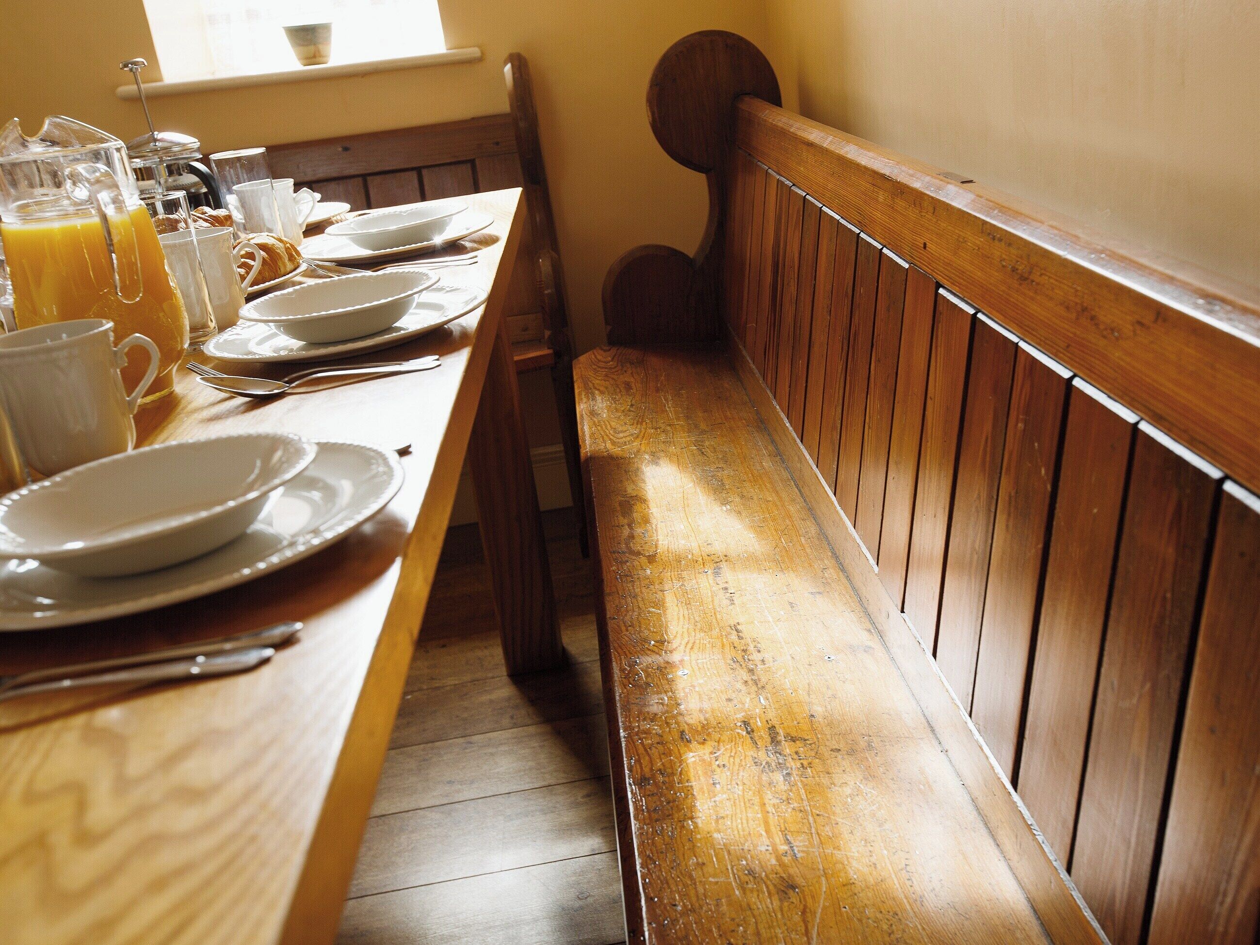 Een houten eettafel met borden, bekers en een karaf sinaasappelsap.