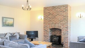 A living room with a brick fireplace, grey sofas, a television, and a chandelier. - 4 bedroom accommodation in Freshwater East near Pembroke (Freshwater East near Pembroke)
