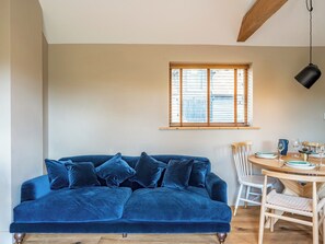 A cozy room with a blue velvet sofa, a wooden dining table with chairs, and a window with blinds. - South Stable at Crabtree Farm - UKC5375 (Hastingleigh)