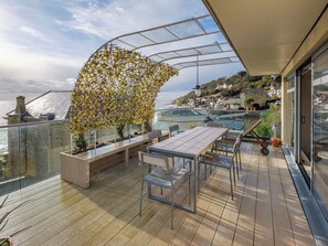 A wooden deck with a table and chairs, a glass balustrade, and a view of the sea and buildings. - 3 bedroom accommodation in Ventnor (Ventnor)