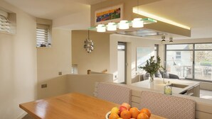 Eine moderne Küche mit einem Holzespeisetisch, einer Obstschale und Blick ins Freie durch große Fenster.