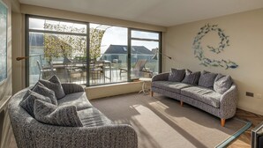 Ein modernes Wohnzimmer mit großem Fenster, einer Couch, einem Sessel und Wandbildern mit Fischmotiven.