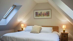Une chambre avec une lucarne, un lit avec une literie blanche, deux lampes de chevet et un tableau accroché au mur.