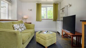 Ein Wohnzimmer mit einer Couch, einem Couchtisch, einem Fernseher und einem Fenster mit Vorhängen.