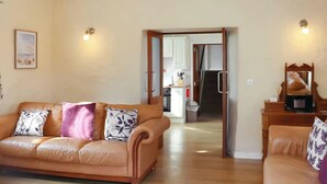 A living room with a brown leather sofa, a wooden cabinet, and a kitchen visible through an open doorway. - 2 bedroom accommodation in Freshwater East near Pembroke (Freshwater East near Pembroke)
